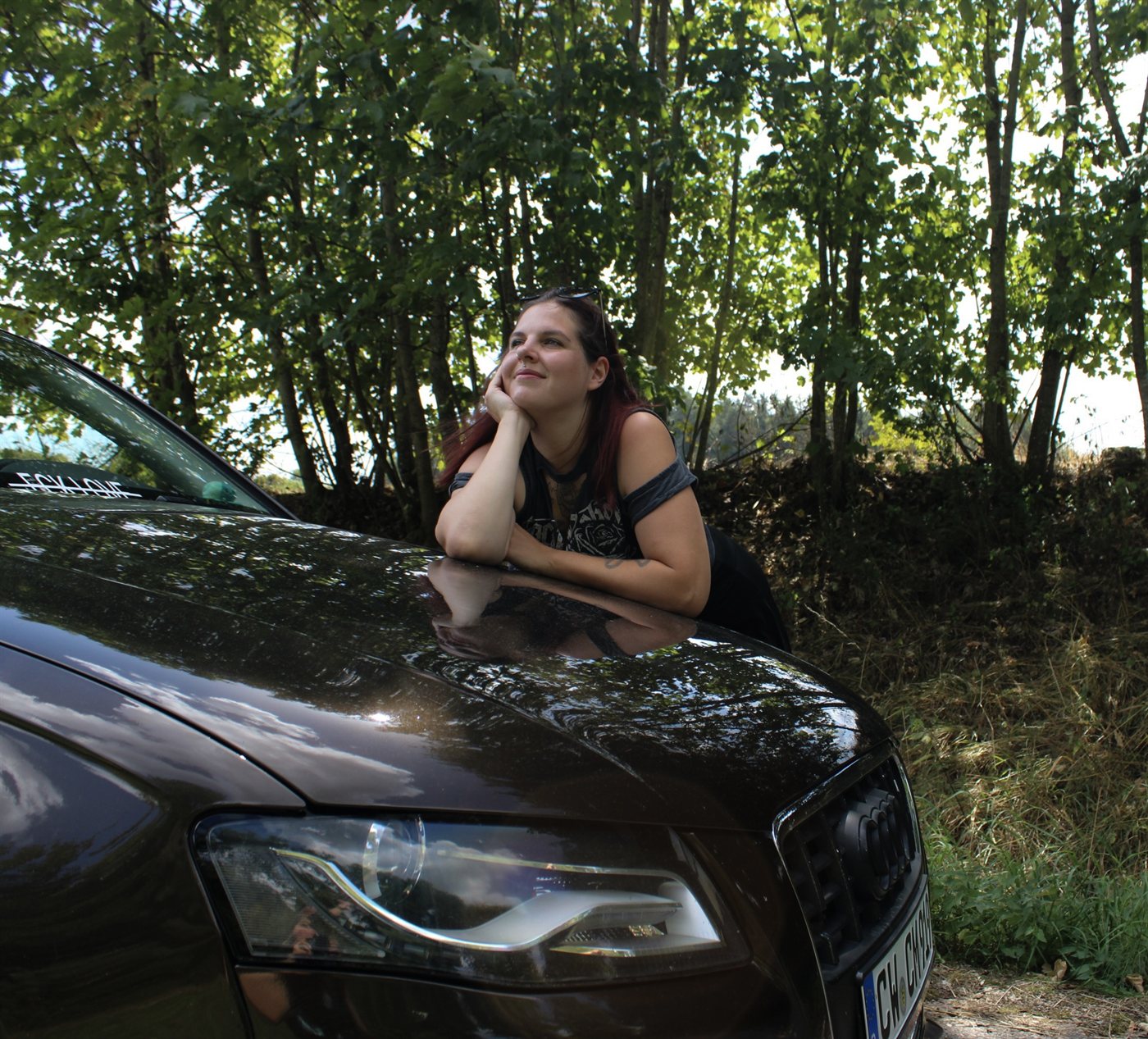 Lilli lehnt lachend auf der Motorhaube eines Audi, im Hintergrund ein Waldweg