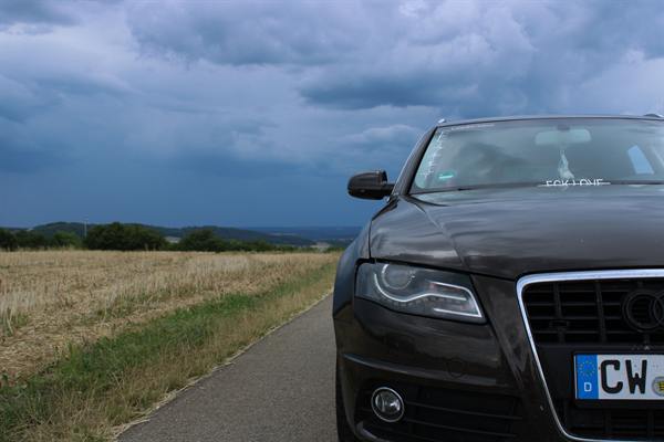 Auto auf einem Feldweg unter dramatischem Wolkenhimmel