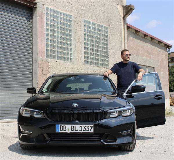 Mann steht neben einem schwarzen BMW vor einer Halle