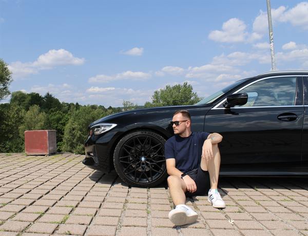 Mann sitzt entspannt neben seinem Auto