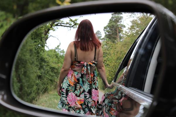 Frau im Blumenkleid gespiegelt im Seitenspiegel eines Autos