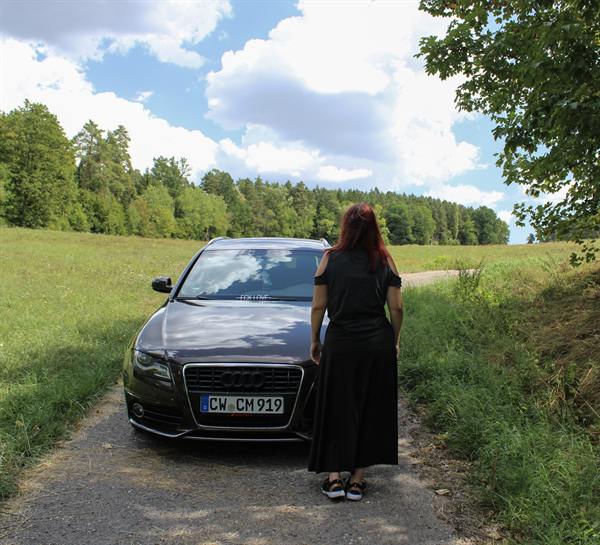 Frau geht neben einem Auto durch ein Feld